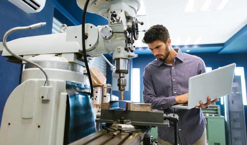 A young latin engineer calibrating a large drill with his laptop in his shop