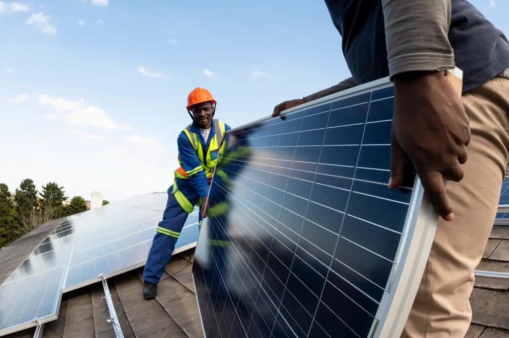 Team of blue collar workers installing solar panel on roof of building